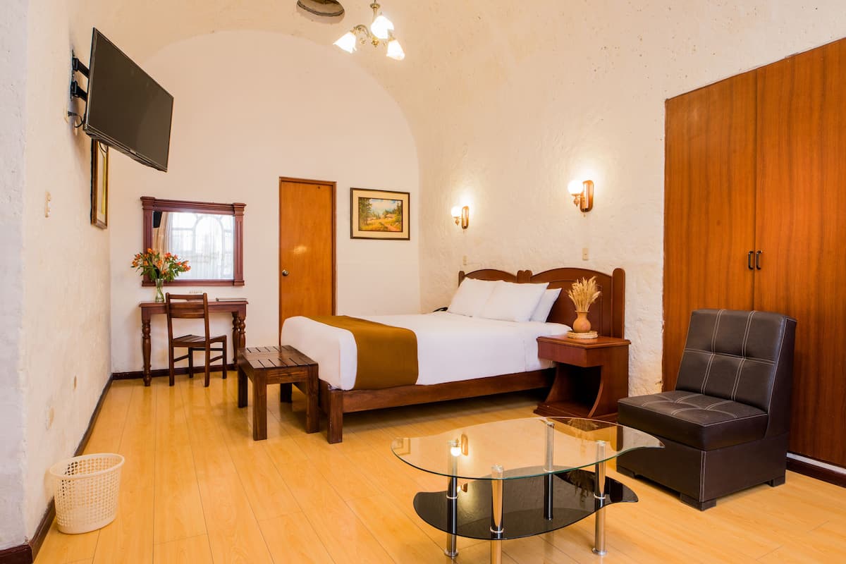 Una habitación de hotel con cama, escritorio, silla, mesa de centro de vidrio y armario.