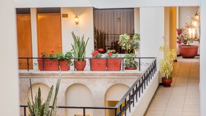 Un hall de hotel con una escalera central, plantas en macetas y vistas del interior del edificio.