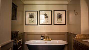 A bathroom with a freestanding bathtub, framed architectural drawings on the wall, and a gold-colored faucet.