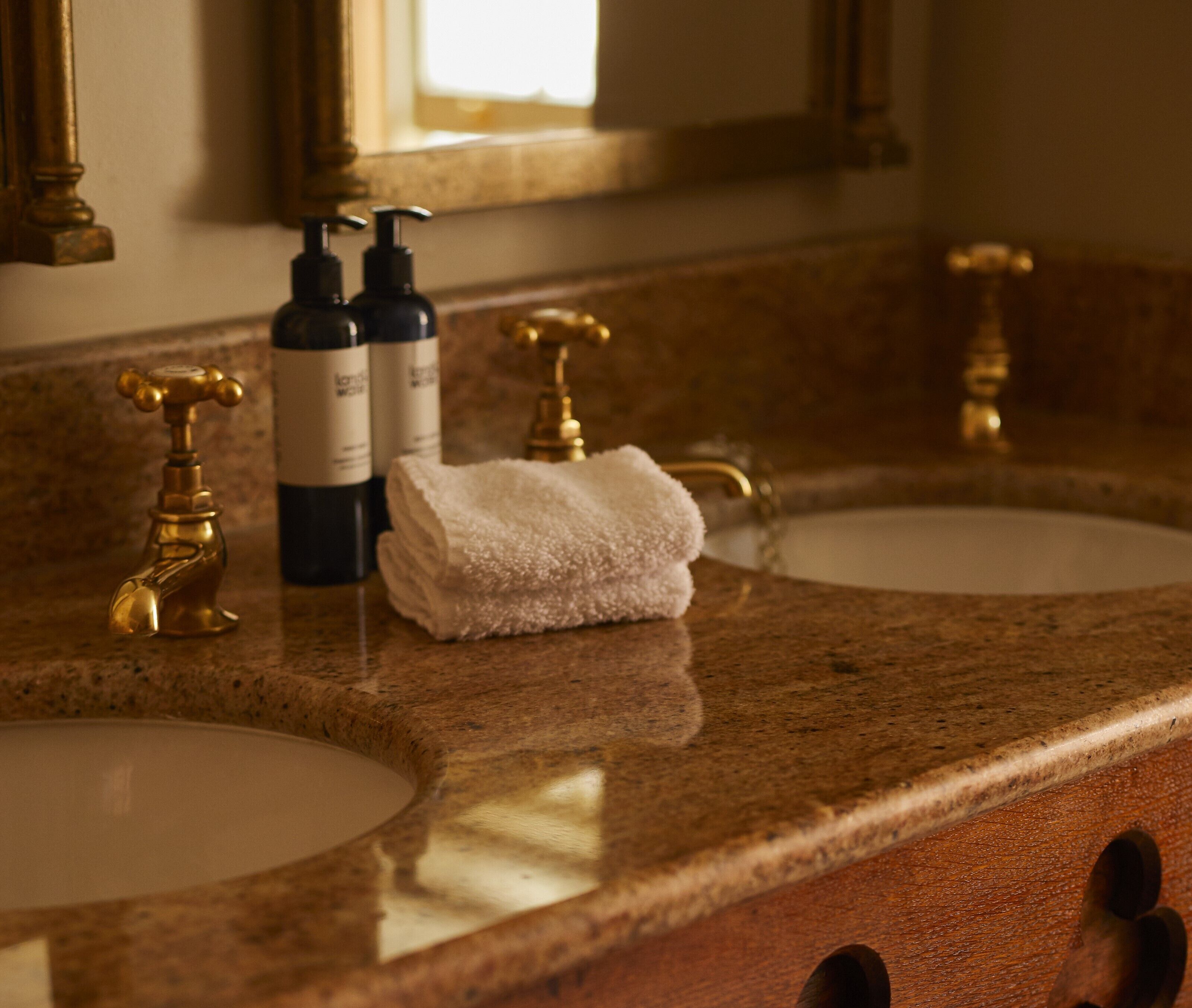 A bathroom with two sinks, gold faucets, and a white towel on the counter.
