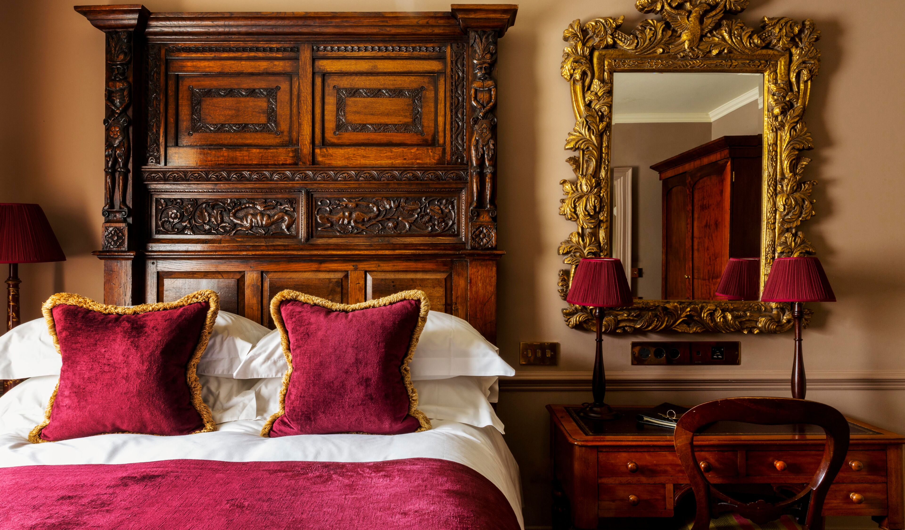Un dormitorio con cabecera de madera, dos almohadas rojas, un espejo con marco decorativo y un escritorio con cajones.