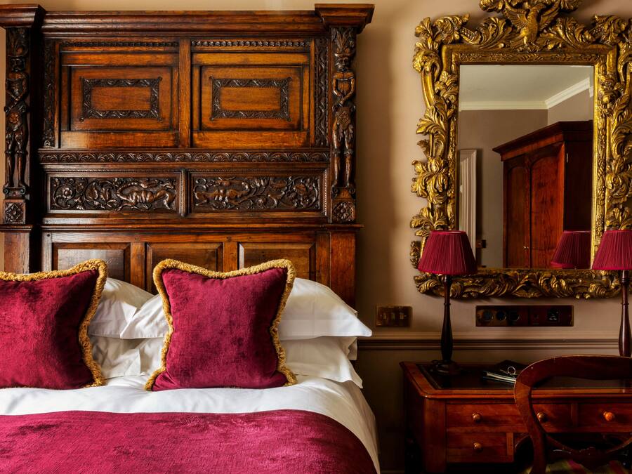 Un dormitorio con cabecera de madera, dos almohadas rojas, un espejo con marco decorativo y un escritorio con cajones.