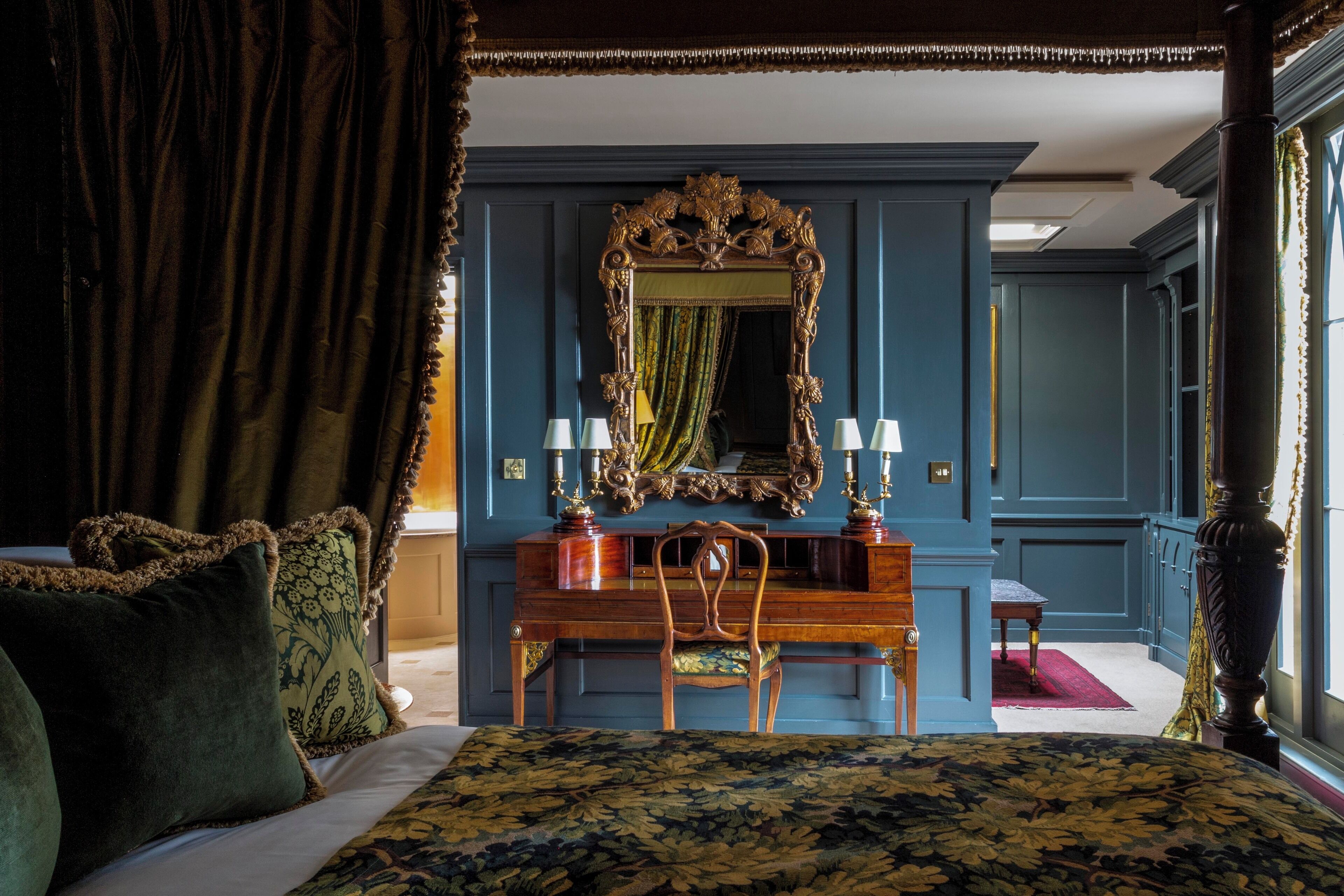 A bedroom with a large bed, a wooden dresser, a mirror, and a desk with lamps.