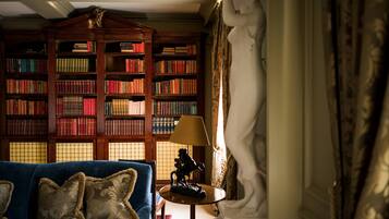 Een kamer met een blauwe bank, een kleine tafel met een lamp en een grote boekenkast vol boeken.