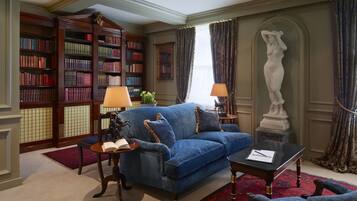 A library with bookshelves, a blue sofa, a red rug, and a statue.
