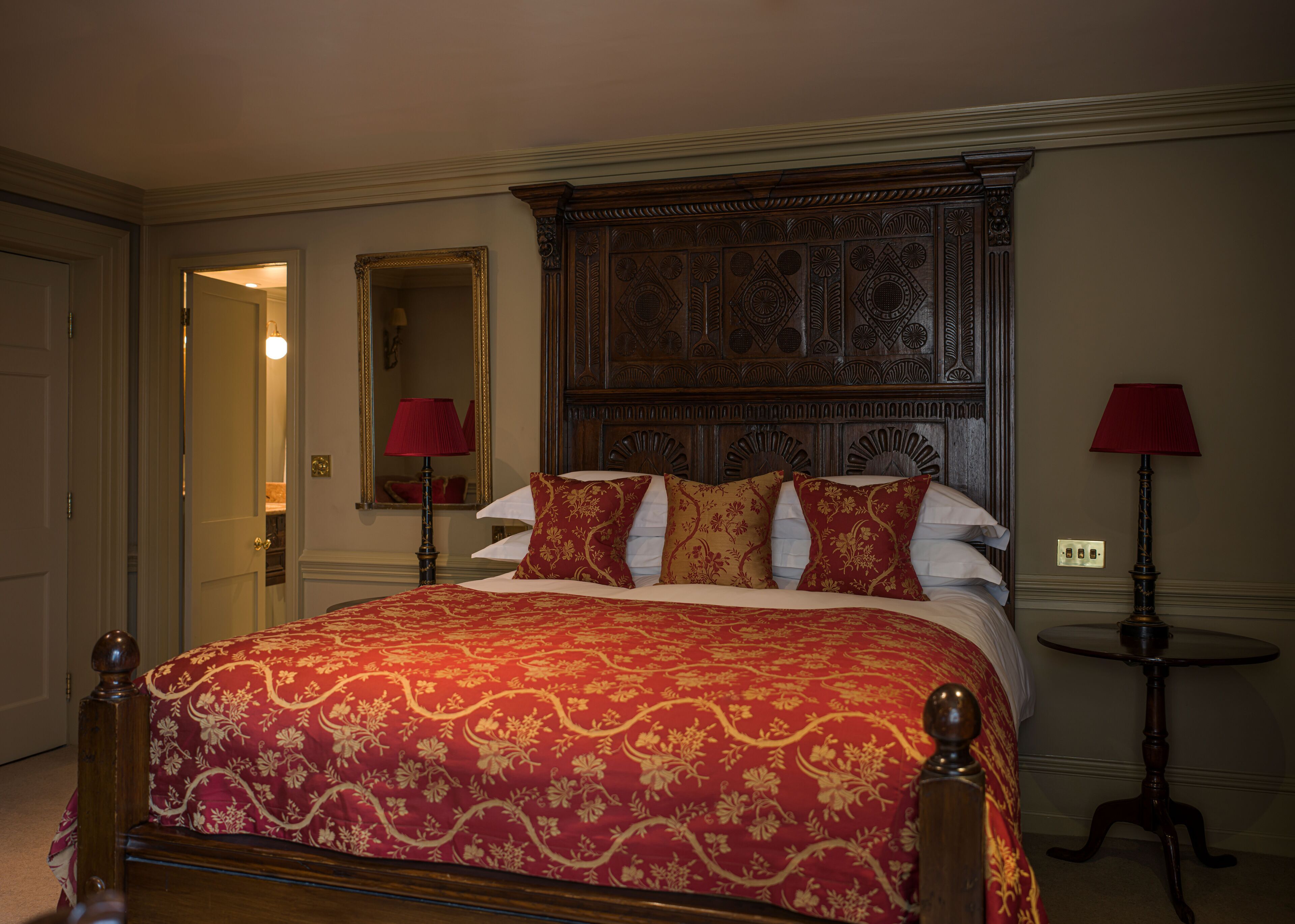 Une chambre d’hôtel avec un grand lit, une tête de lit décorée, deux tables de chevet avec des lampes et un miroir au mur.