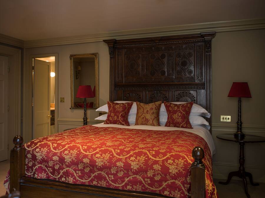 Une chambre d’hôtel avec un grand lit, une tête de lit décorée, deux tables de chevet avec des lampes et un miroir au mur.