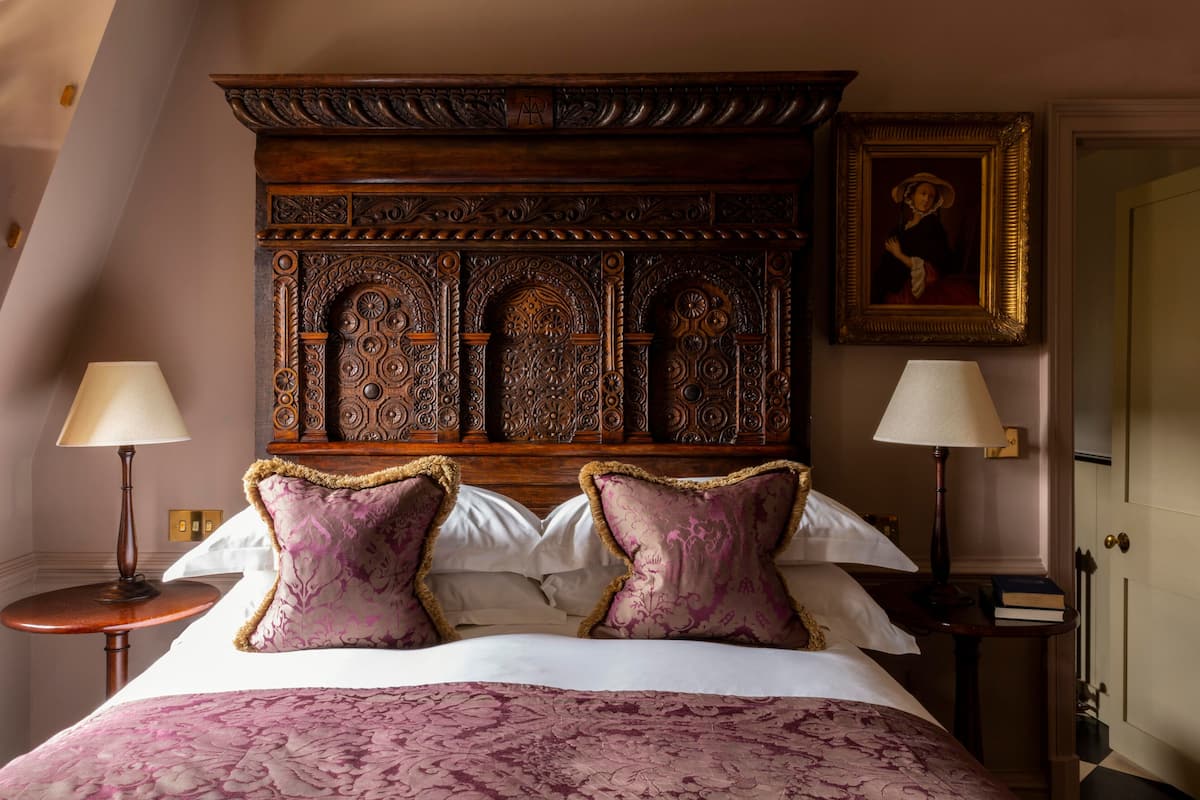 A bedroom with a large bed, ornate headboard, two bedside tables with lamps, and a framed picture on the wall.
