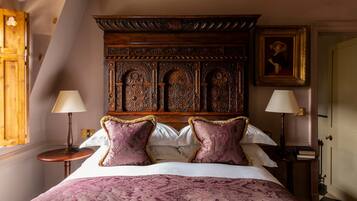 A bedroom with a large bed, ornate headboard, two bedside tables with lamps, and a framed picture on the wall.