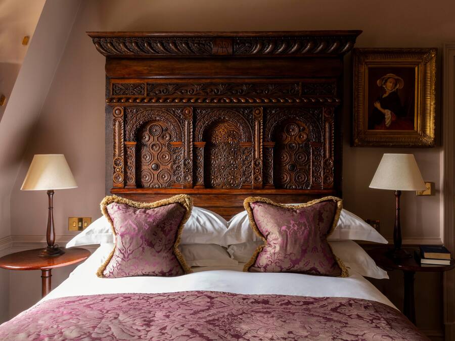 A bedroom with a large bed, ornate headboard, two bedside tables with lamps, and a framed picture on the wall.