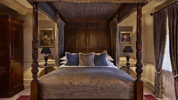 A four-poster canopy bed with a floral bedspread, two nightstands with lamps, and a red patterned rug.