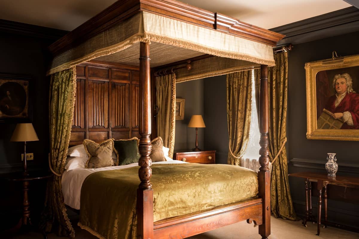 A four-poster canopy bed with a green bedspread, wooden headboard, and matching curtains.