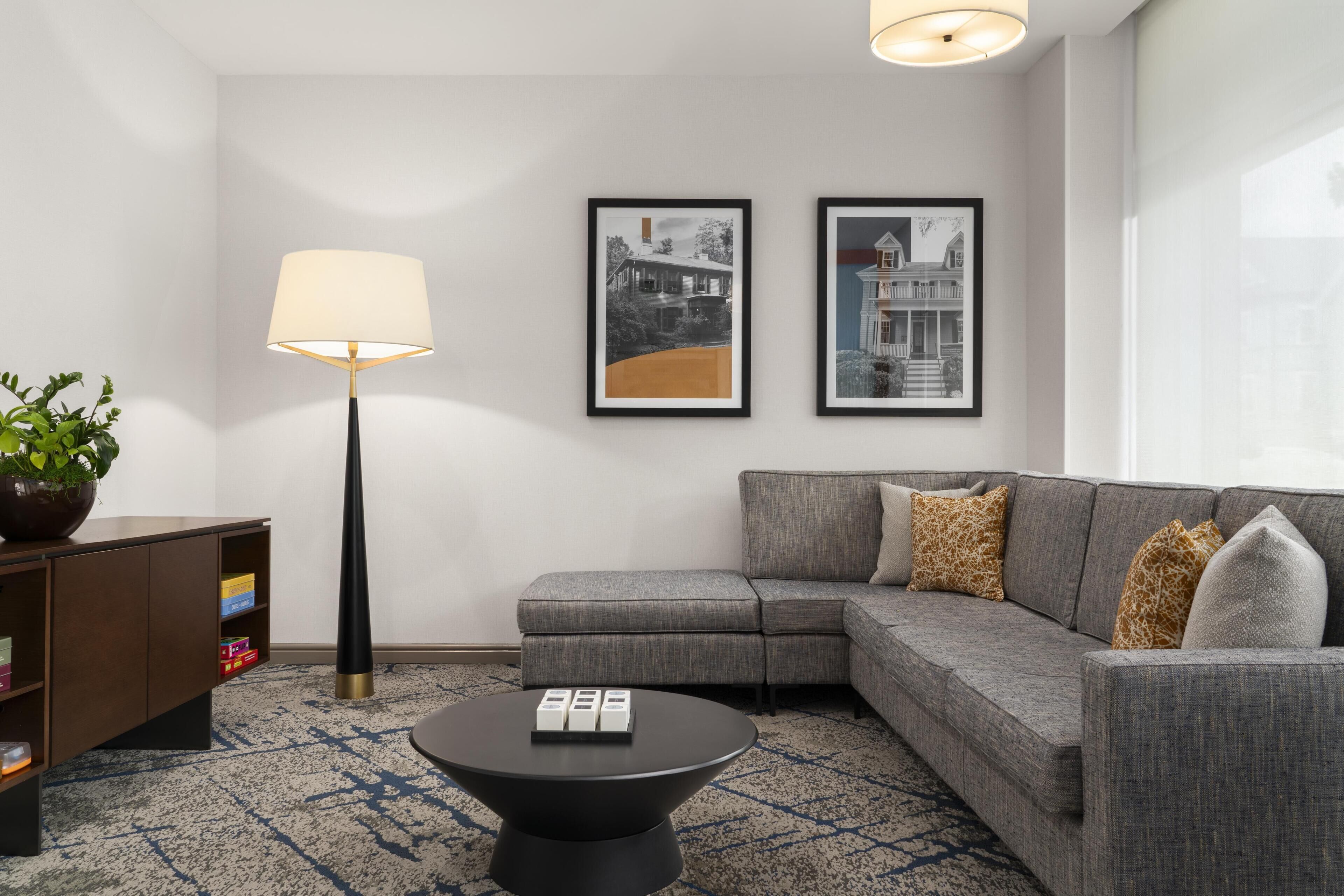 A modern living room with a grey sectional sofa, a black coffee table, a floor lamp, and two framed pictures on the wall.