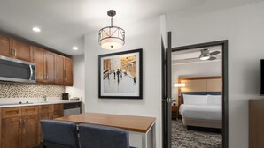 A compact hotel room with a kitchenette, a dining area, a bed, and a hallway leading to a bathroom. - Homewood Suites by Hilton Boston Brookline-Longwood Medical (Brookline)