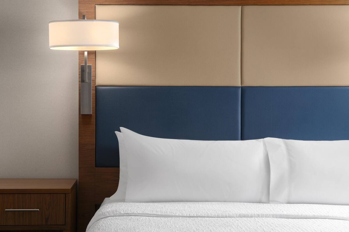 Quarto de hotel com cama, mesa de cabeceira, luminária e cabeceira com design azul e bege.