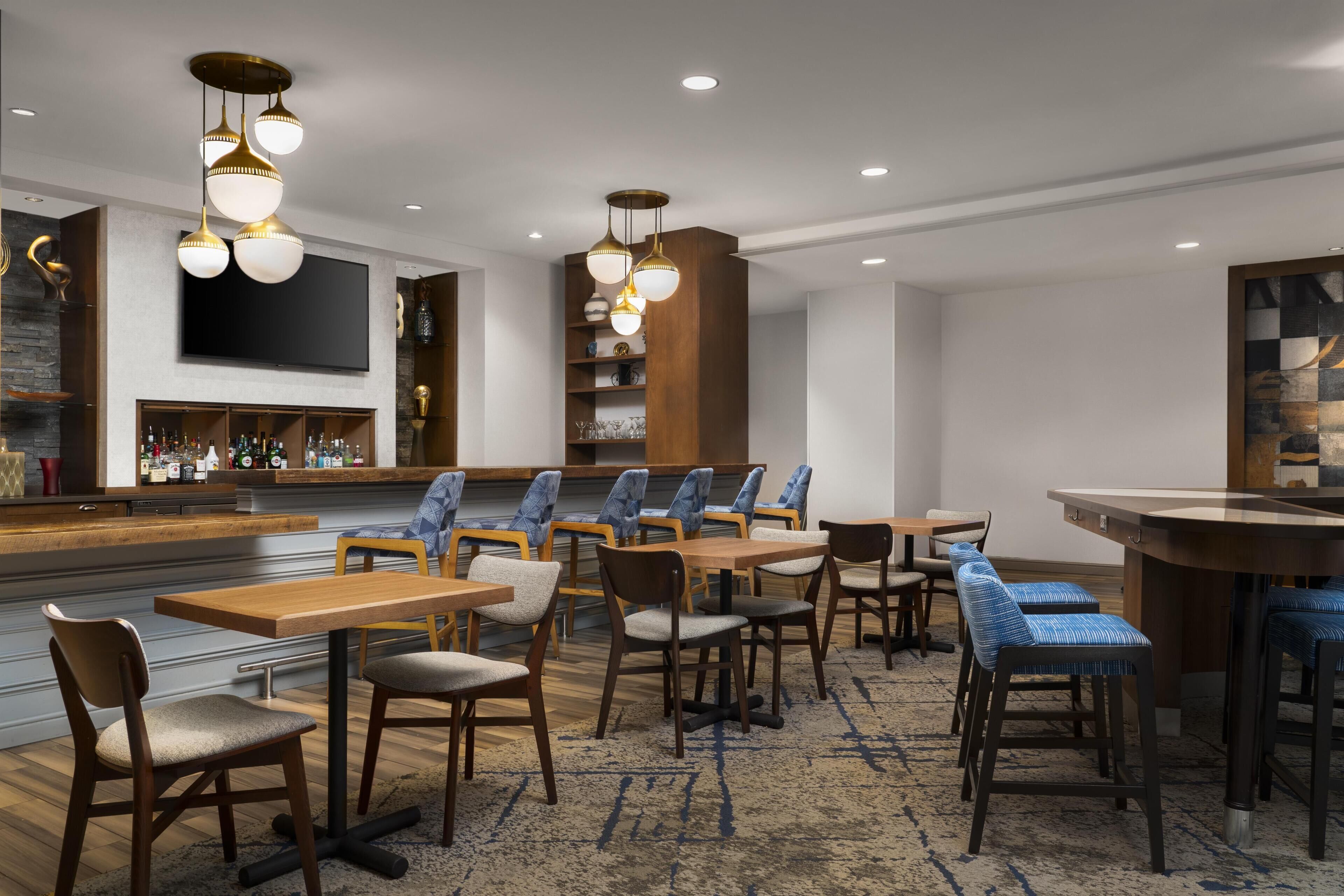 A modern hotel lobby with a bar area, seating arrangements, and a large flat-screen TV.