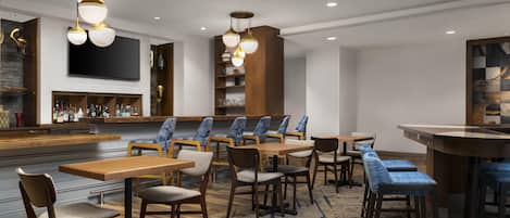 A modern hotel lobby with a bar area, seating arrangements, and a large flat-screen TV.