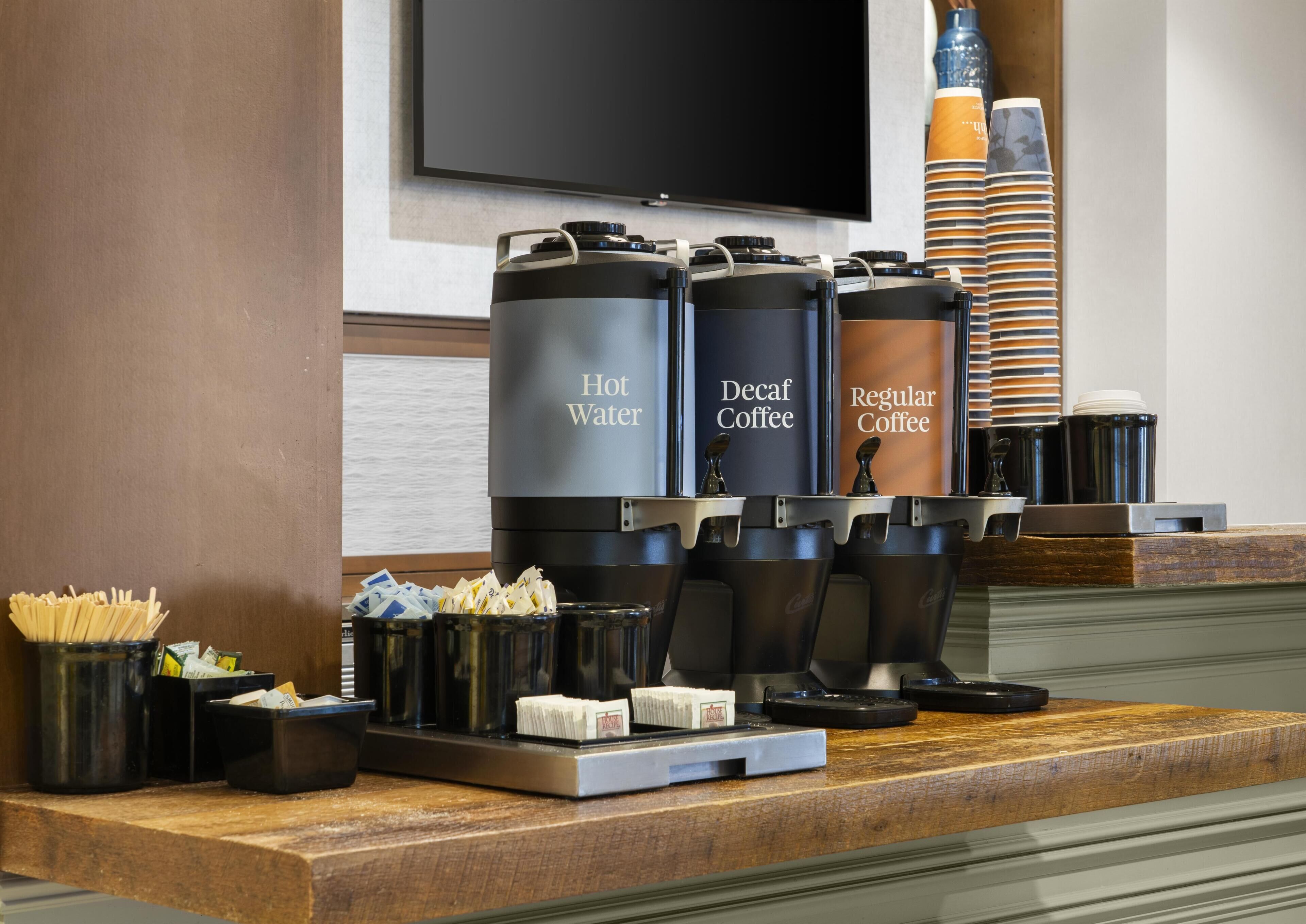 Una estación de café con dispensadores etiquetados para agua caliente, café descafeinado y café regular.
