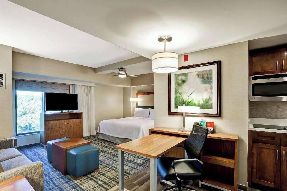 A hotel room with a bed, a desk, a chair, a television, a window, and a kitchenette.