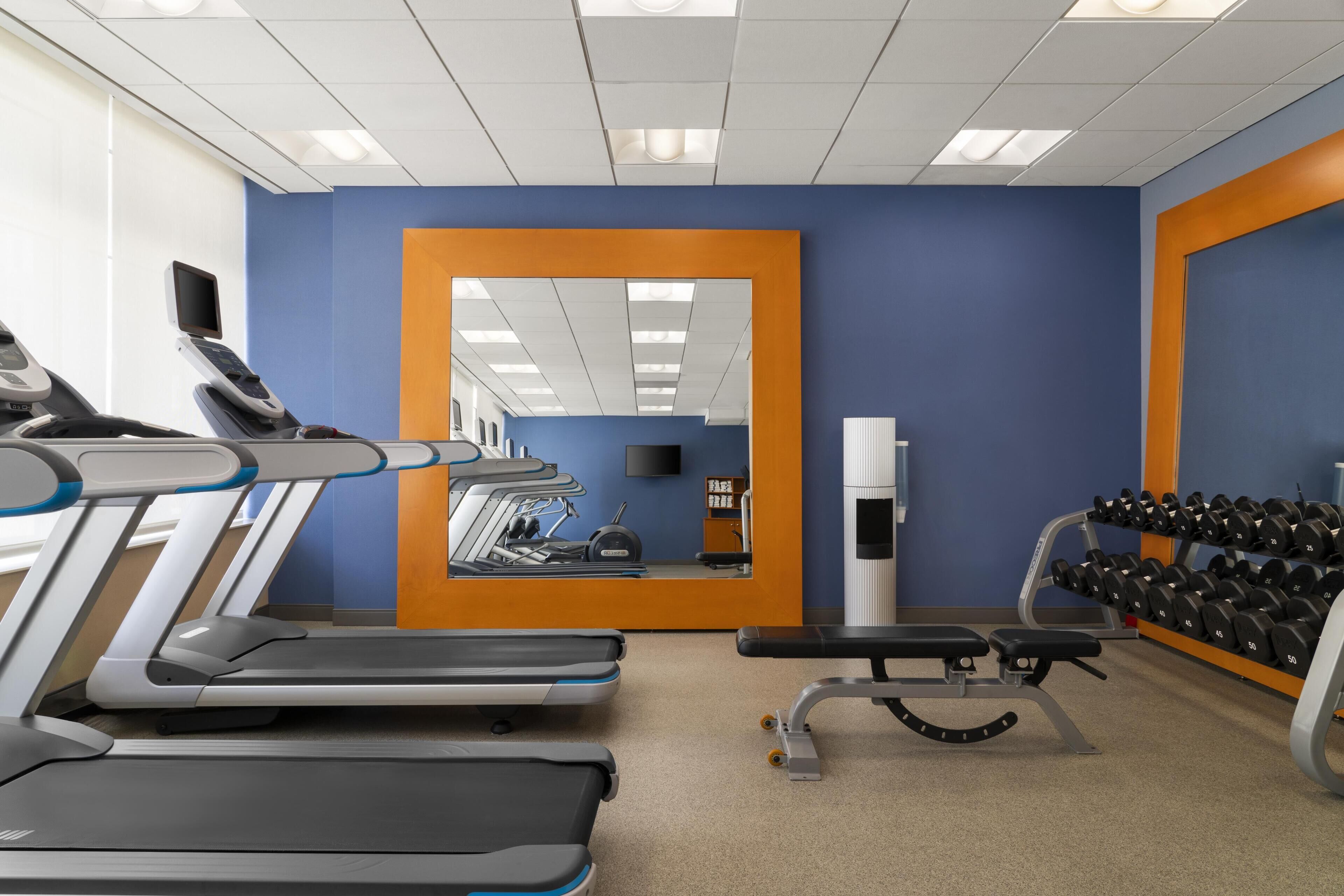 Une salle de sport équipée de tapis de course, d’un banc et d’un porte-haltères.