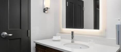 A modern bathroom with a white sink, dark wooden vanity, and a large mirror with integrated lighting.