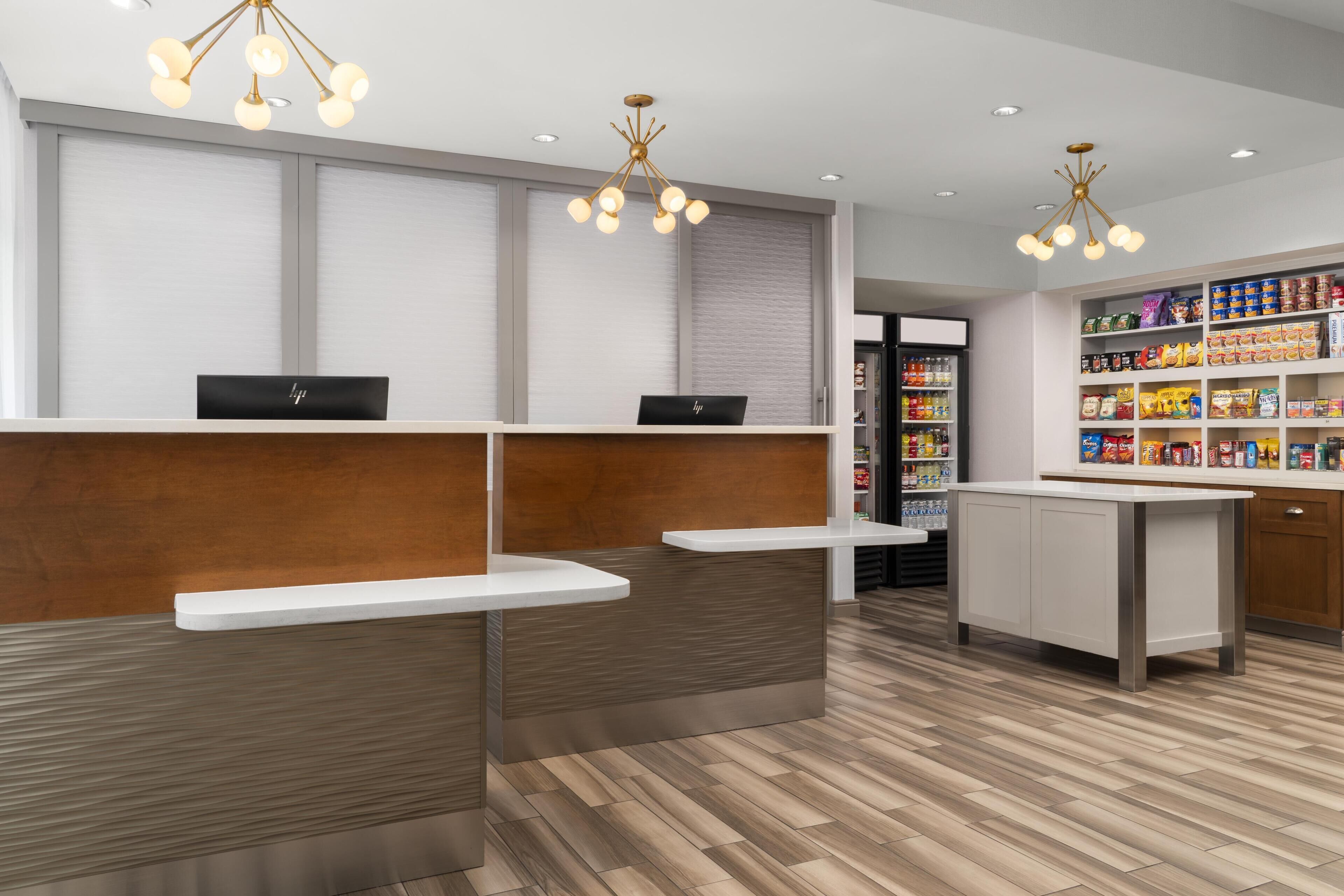 A modern reception area with a wooden reception desk, white counter, and a food display.