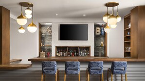 A bar area with a flat-screen TV, wooden bar counter, and three patterned bar stools. - Homewood Suites by Hilton Boston Brookline-Longwood Medical (Brookline)