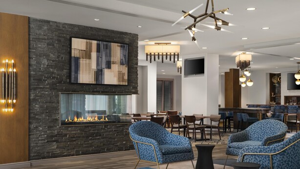 A modern hotel lobby with a stone fireplace, blue patterned chairs, a bar area, and a large abstract painting on the wall. - Homewood Suites by Hilton Boston Brookline-Longwood Medical (Brookline)