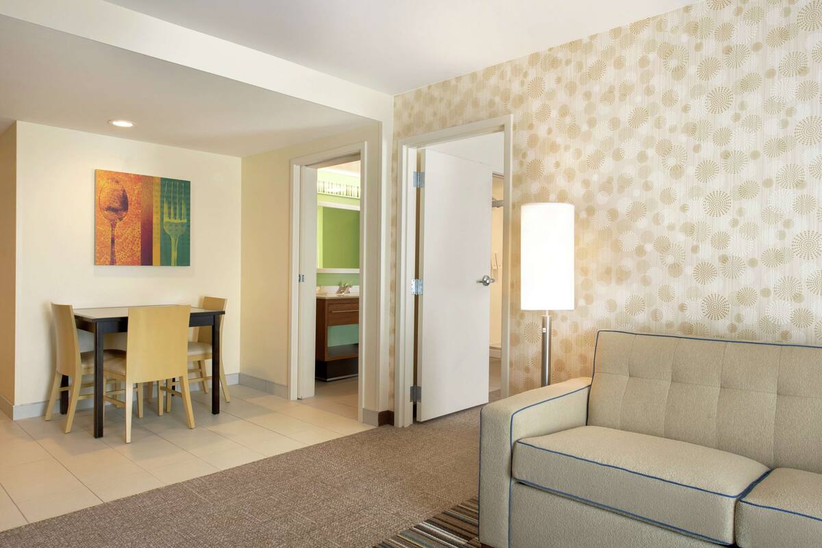 Een hotelkamer met een eethoek, een bank, een lamp en een deur naar een badkamer.