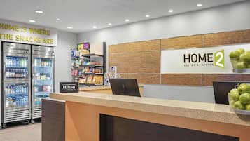 A hotel reception area with a counter, vending machines, and a sign for 'HOME 2 Suites by Hilton.'