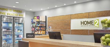 Un espace d’accueil d’hôtel comprenant un comptoir, des distributeurs automatiques et un panneau indiquant « HOME 2 Suites by Hilton ».