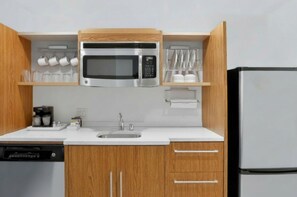 Une cuisine moderne équipée d’un four à micro-ondes encastré, d’un évier et de meubles de rangement en bois.