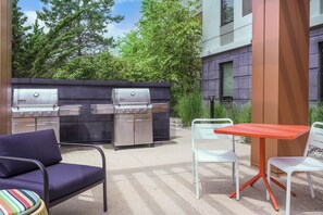 Eine Terrasse im Freien mit einem Weber Summit Gasgrill und einem Weber Summit Räucherofen, zwei weißen Stühlen und einem roten Tisch.