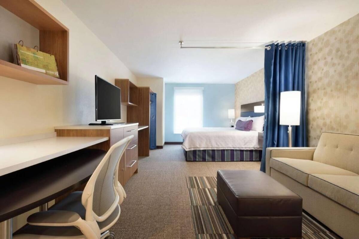 Een hotelkamer met een bed, een bureau met stoel, een televisie, een bank en een lamp.