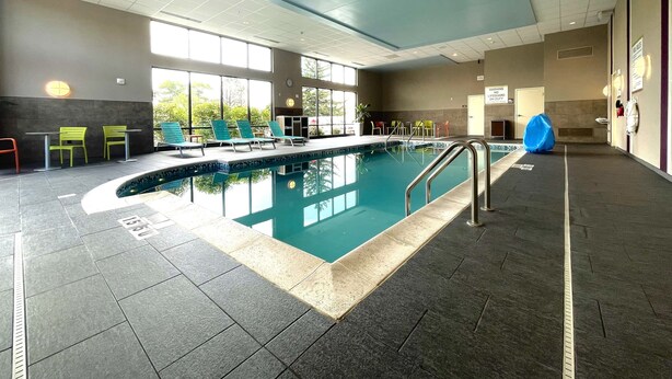 An indoor swimming pool with a tiled floor, a pool ladder, and chairs around the pool. - Home2 Suites by Hilton Milwaukee Airport (Milwaukee)