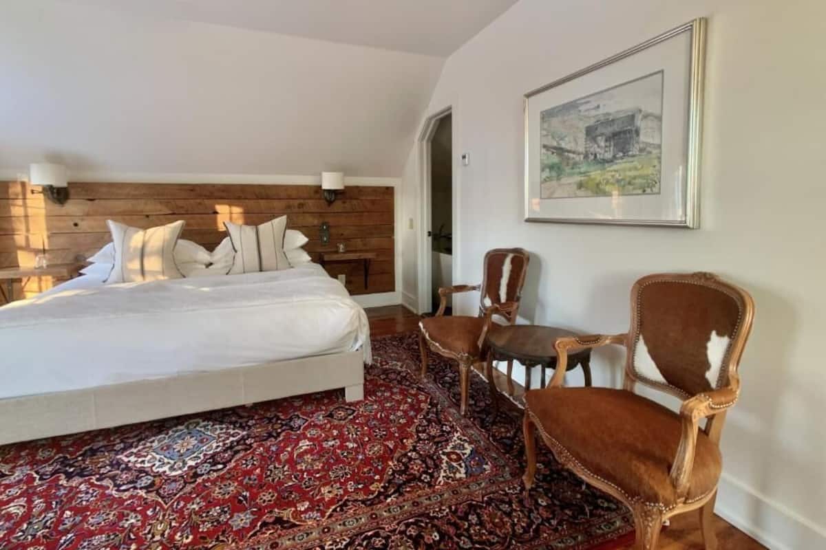 A bedroom with a large bed, a wooden headboard, a red patterned rug, and a framed picture on the wall.