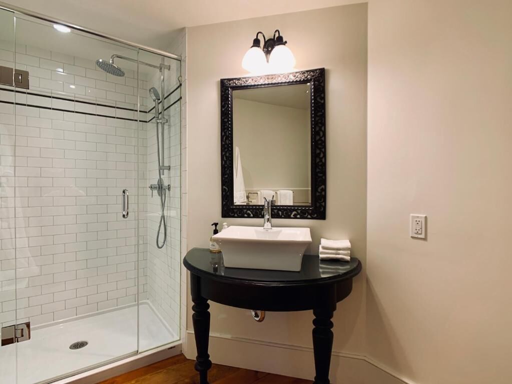 Un baño con ducha de vidrio, lavamanos blanco y tocador negro.