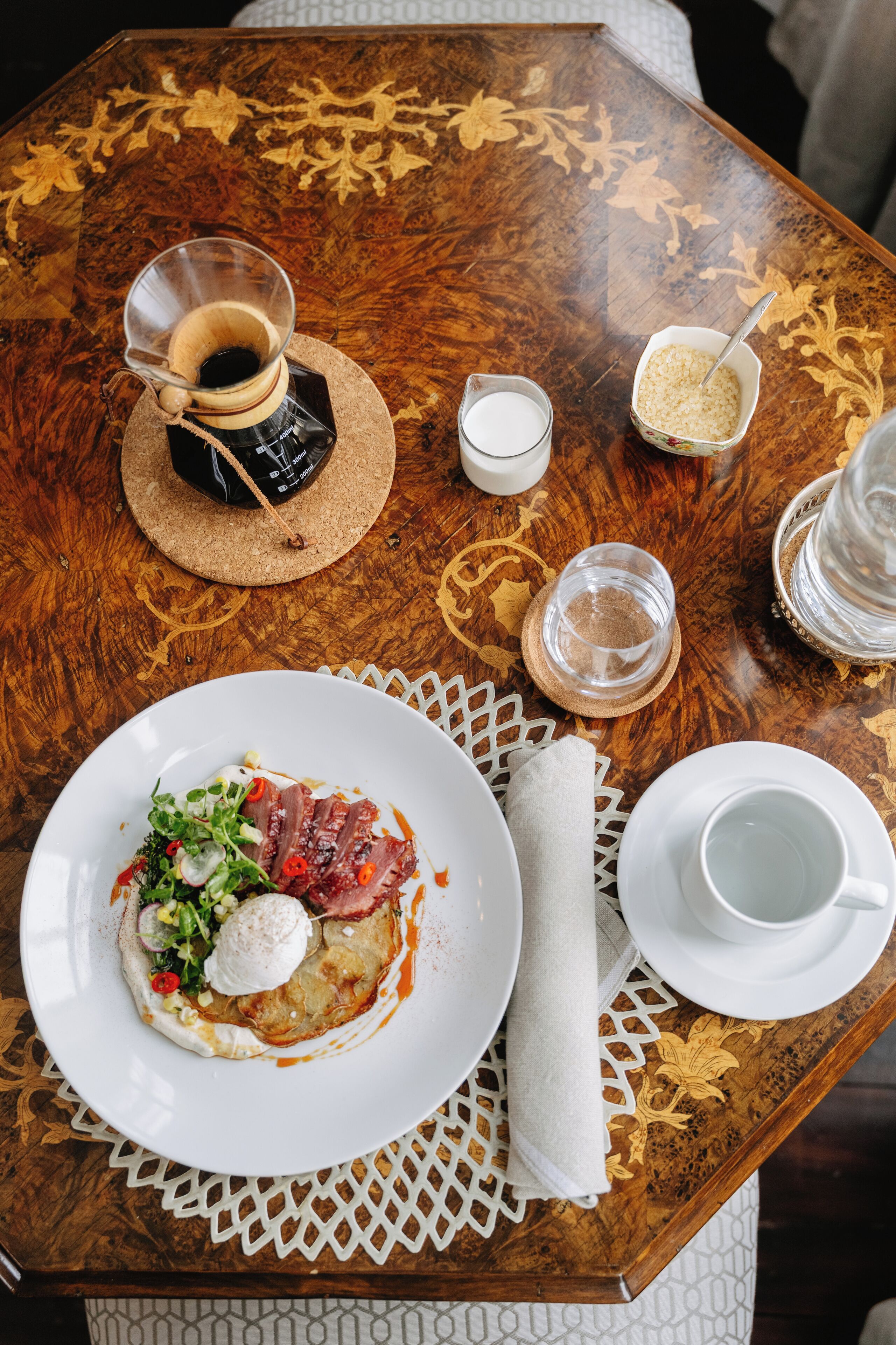 Una mesa de madera con un plato de comida, una cafetera y una taza.