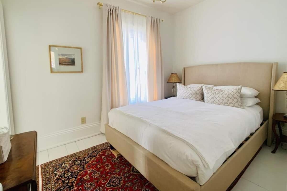 A neatly arranged bedroom with a large bed, a bedside table, a lamp, and a framed picture on the wall.
