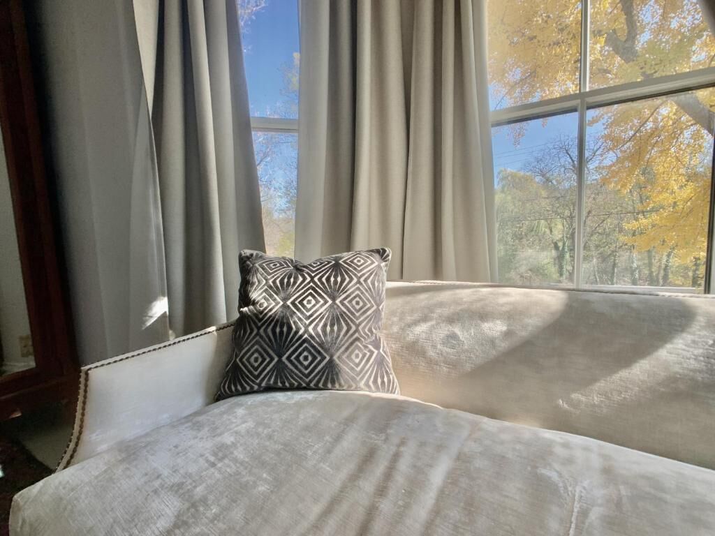 A room with a large window, a patterned pillow, and a light-colored sofa.