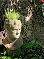 A stone statue with a green top, set against a tree trunk.