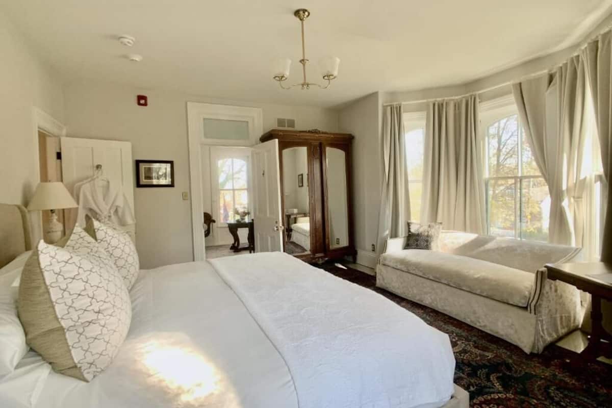 A bedroom with a large bed, a sofa, a mirror, and a window with curtains.