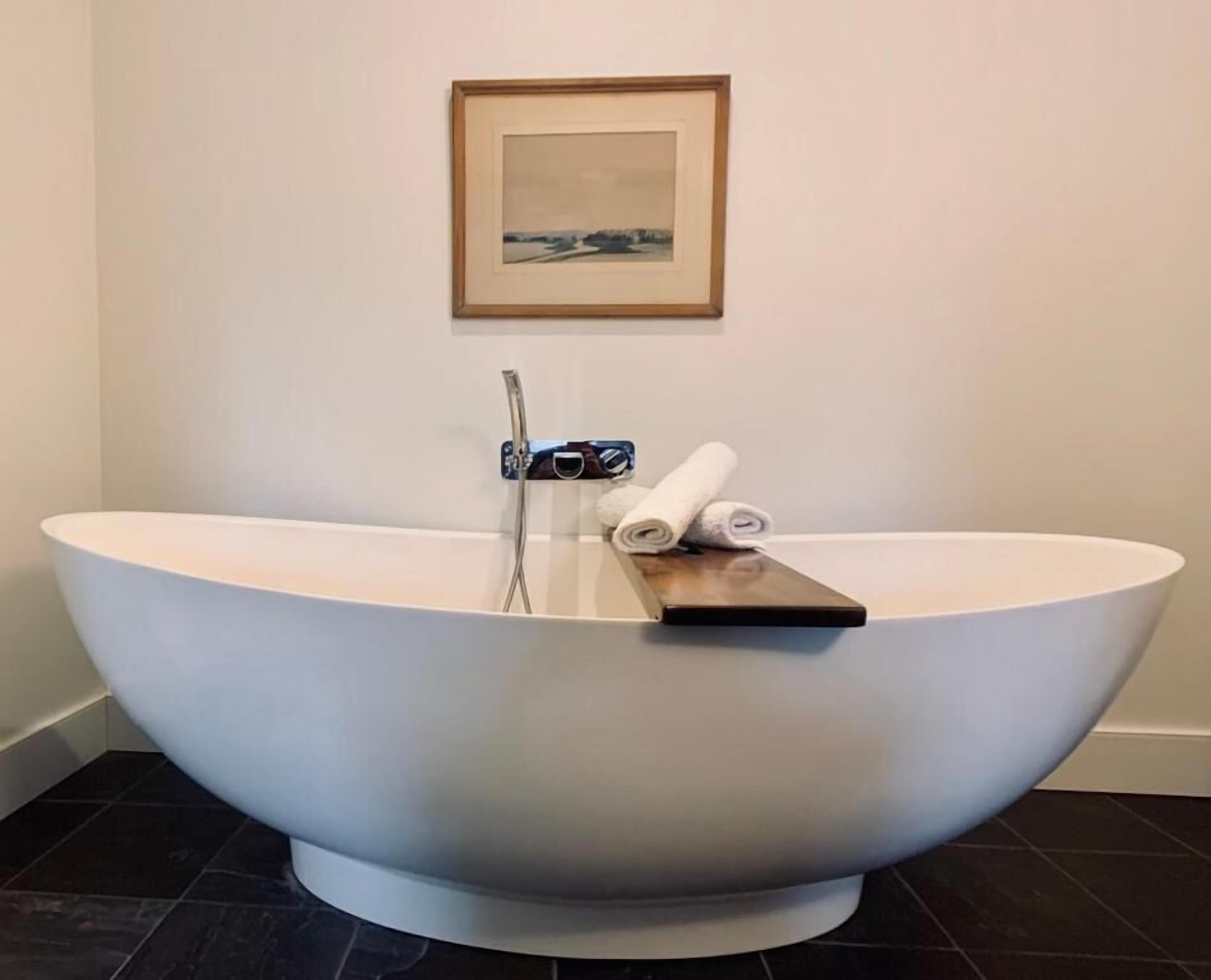 A modern bathroom with a freestanding bathtub, a framed picture on the wall, and a towel on the edge of the tub.