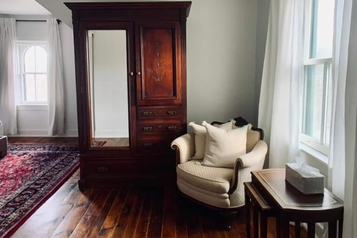 A room with a wooden floor, a large armoire, a cream-colored armchair, and a small table.