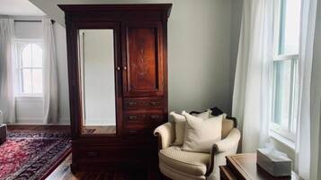 Een kamer met een houten vloer, een grote kast, een beige fauteuil en een kleine tafel.