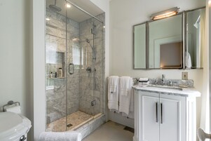 Un baño moderno con ducha acristalada, tocador de mármol y un espejo grande sobre el lavabo.