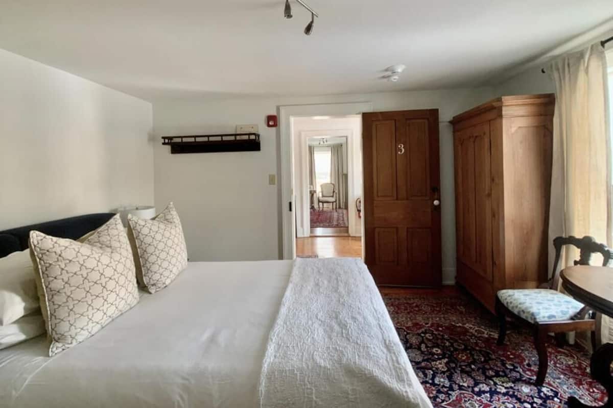 A hotel room with a bed, a wooden wardrobe, a chair, and a small table.