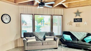 A living room with two sofas, a ceiling fan, and large windows with blinds. - Breakers Boutique Inn (Westport)
