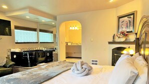 A hotel room with a bed, a black stove, a mirror, a painting, and a fireplace. - Breakers Boutique Inn (Westport)