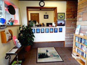 A reception area with a clock, framed pictures, a potted plant, a rug with a lighthouse design, and a bookshelf. - Breakers Boutique Inn (Westport)